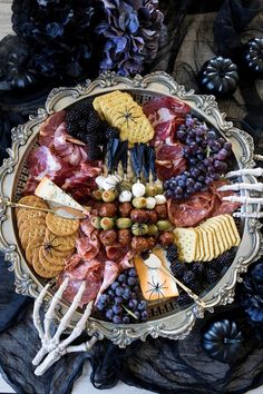 a platter filled with cheese, meats and crackers next to black flowers