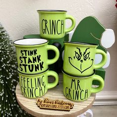 three green mugs sitting on top of a wooden table next to a christmas tree