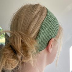 a woman with blonde hair wearing a green knitted headband in front of a window