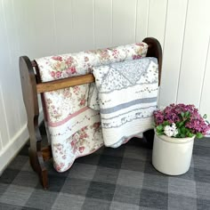 a potted plant sitting next to a blanket on a wooden bench in front of a white wall