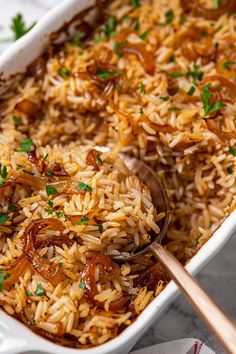 a white casserole dish filled with rice and onions, garnished with parsley