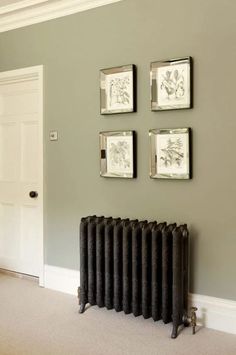 three framed pictures on the wall above a radiator in a room with grey walls