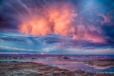 the sky is filled with pink and blue clouds as it sits over a body of water