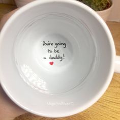 a white bowl with writing on it sitting on a table next to a potted plant