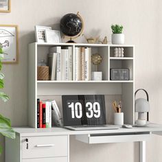 a white desk with a clock on it next to a potted plant and bookshelf