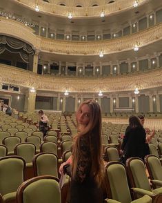 a woman standing in front of a large auditorium filled with green chairs