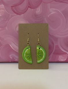 a pair of green earrings with a slice of lime in the middle on a pink background