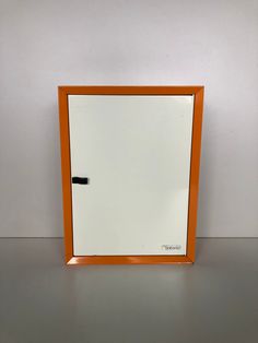 an orange and white framed mirror sitting on top of a table