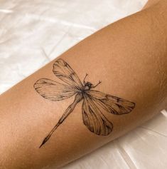 a black and white photo of a small dragonfly tattoo on the right arm,