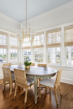 a dining room table with chairs and a potted plant in the center surrounded by windows