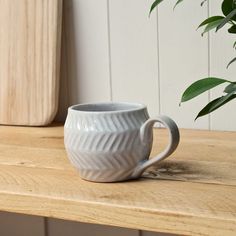 a white coffee cup sitting on top of a wooden table next to a potted plant