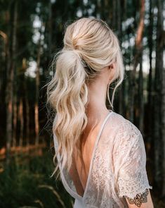 a woman standing in the woods with her back to the camera, wearing a white top