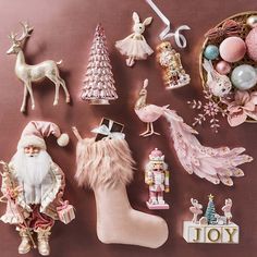 various christmas decorations and figurines are arranged on a table with a pink background