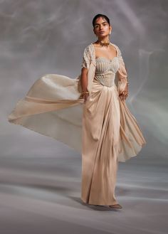 Editor's Note Drape skirt for the win with a beige corset in embellishments matched with embroidered cape. Color: Beige Fabric: Heavy satin, crushed organza Fit type: Corset: fitted Neckline: Sweetheart Components: Corset, cape and skirt Occasion: Cocktail and reception Care: Dry Clean Only About the Designer The crux and essence of the label, Divya Aggarwal, is to challenge and revamp the face of ordinary traditional wear while being customer oriented. Driven by the values of individuality and Beige Corset, Corset And Skirt, Cape Set, Beaded Cape, Embroidered Cape, Blouse Yoke, Draped Skirt, Indian Fashion Designers, Fashion App