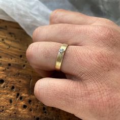 a person's hand wearing a gold ring with a diamond in it on top of a wooden table