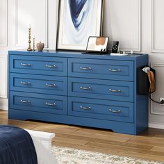 a blue dresser in a white room with a painting on the wall