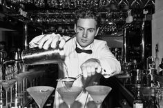 a man in a bow tie is making a drink at a bar with martini glasses on the counter