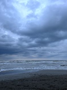 a person walking on the beach with a surfboard under an overcast cloudy sky