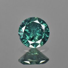 a green diamond sitting on top of a reflective surface in front of a gray background