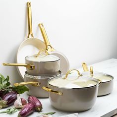 three pots and two pans with gold handles on the side, sitting next to each other