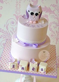 a three tiered cake with an owl on top and purple ribbon around the edges