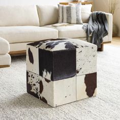 a cow hide ottoman sitting on top of a rug in front of a white couch