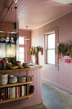 a kitchen with pink walls and wooden shelves filled with plates, bowls and utensils