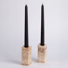 two black candles sitting on top of each other next to each other in cement blocks