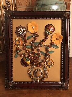 a wooden frame with flowers and beads in it on a table next to a vase