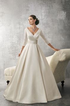 a woman in a white wedding dress standing next to a couch with her hands on her hips