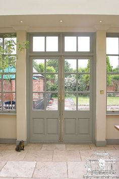 two cats sitting on the floor in front of double doors that lead to a patio