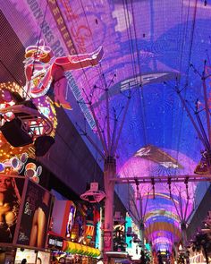 the inside of a shopping mall with people walking around and lots of neon lights on the ceiling