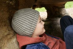 a young boy wearing a hat and jacket sitting in a tree trunk with his feet up