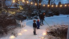 a woman and two children are walking in the snow with lights strung over their heads