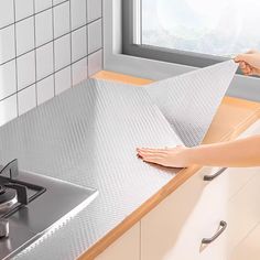 a woman is cleaning the counter top in her kitchen with a towel on it and a window behind her