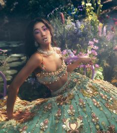 a woman in a green and gold dress posing for the camera with flowers behind her