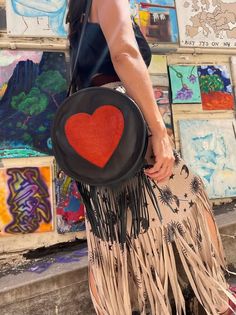 Girl wearing black crop top & tan and black sun & moon print fringe hem skirt carrying hand crafted round black leather purse with red heart center and long fringe along bottom of purse Purse With Fringe, Leather Fringe Purse, Heart Center, Fringe Purse, Unique Purses, Pink House, Pink Houses, Round Leather, Boutique Design