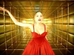 a woman in a red dress standing in front of a gold wall with her arms outstretched