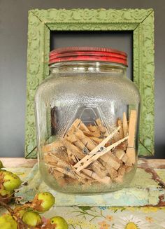 a glass jar filled with lots of wooden clothes pins next to a green frame on a table