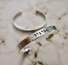 two silver bracelets with the word hebrew written on them, sitting on a marble surface