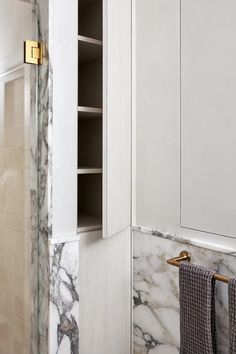 a bathroom with marble walls and white cabinetry, gold handles on the towel rack