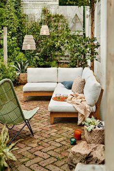 an outdoor living area with couches, chairs and plants on the brick flooring