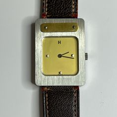 Herms Stainless Steel And Gold Plated Manual Wind Watch. Bezel - Stainless Steel With Vertical Brushed Finish. Rectangular Gold Colored Plate With Two Screws At Top Of Bezel. Dial - Champagne Gold Color, H At 12:00, Pyramid Shaped Markers At 3,6 And 9:00. Face Measures 16 X 15 Mm. Case - Measures 29 X 21 Mm. Case Back Stamped With Hermes And 1751. Strap - Brown Fine Grained Leather On Exterior And Gold Smooth Leather On Interior. Stamped M And Bracelet Hermes. 16mm Lug Width- Strap Attachment. L Silver Leather Watch For Evening, Silver Leather Evening Watch, Vintage Leather Watch With Diamond Hour Markers, Bracelet Hermes, Champagne Gold Color, Hermes Accessories, Champagne Gold, Leather Band, Smooth Leather