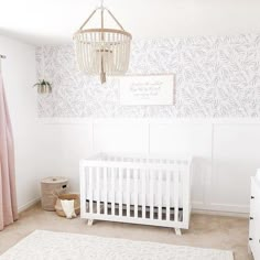 a baby's room with a white crib, pink curtains and a chandelier