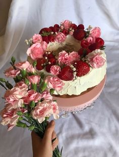 someone is holding a cake with strawberries and flowers on it