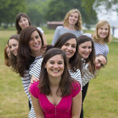 a group of young women standing next to each other in a grassy field with trees behind them