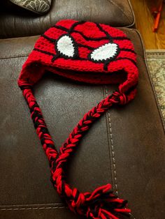 a crocheted red hat with white eyes on it sitting on top of a brown leather couch