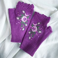 two purple knitted mittens with flowers on them sitting on a white cloth covered surface