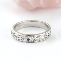 a white gold wedding ring with blue sapphire stones on it's side, sitting next to a pink flower