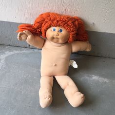 a baby doll with red hair and blue eyes laying on the ground next to a wall